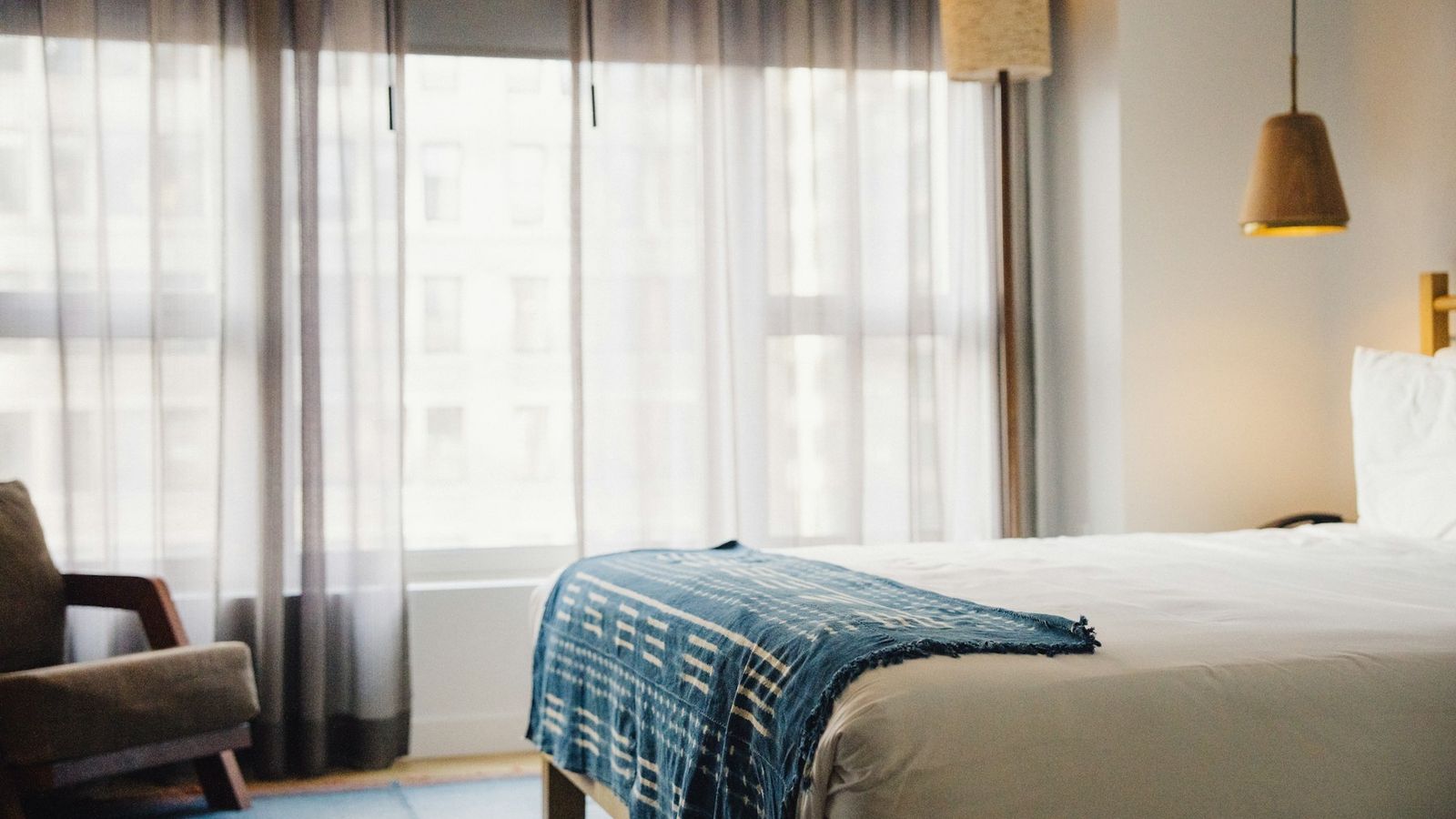 Bright, calm hotel room with a made bed and sheer curtains